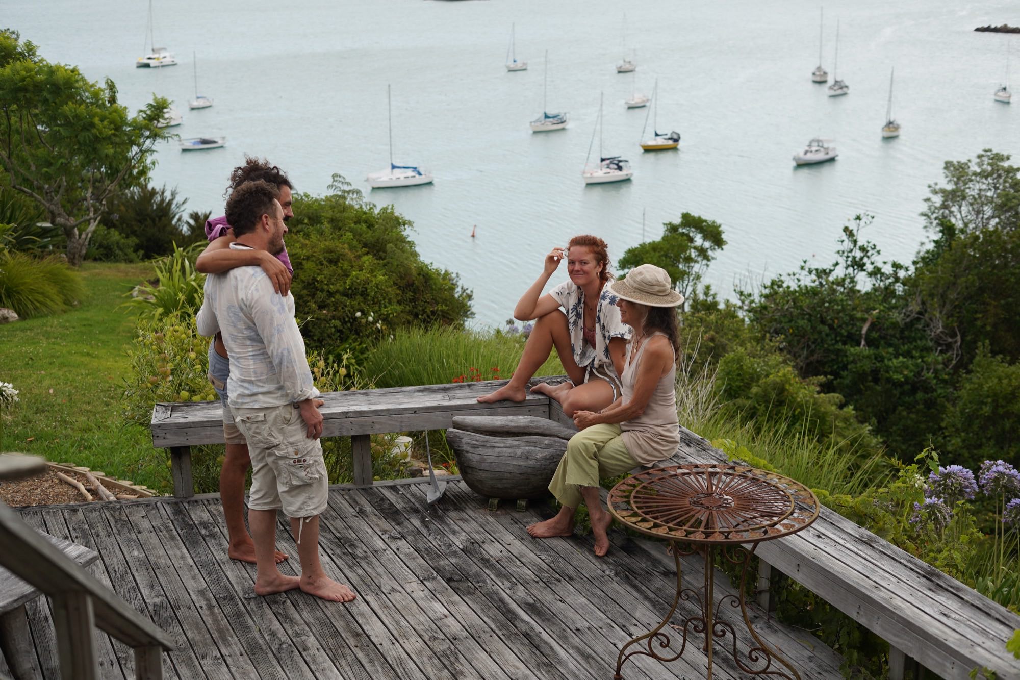 Four people talking on a weathered wooden deck above a harbour full of moored boats