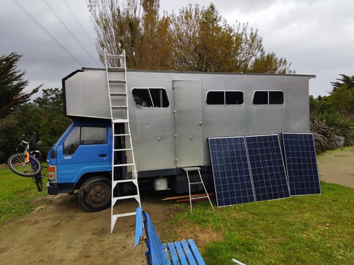 A house truck parked on grass with solar panels leaning against it, ready to install